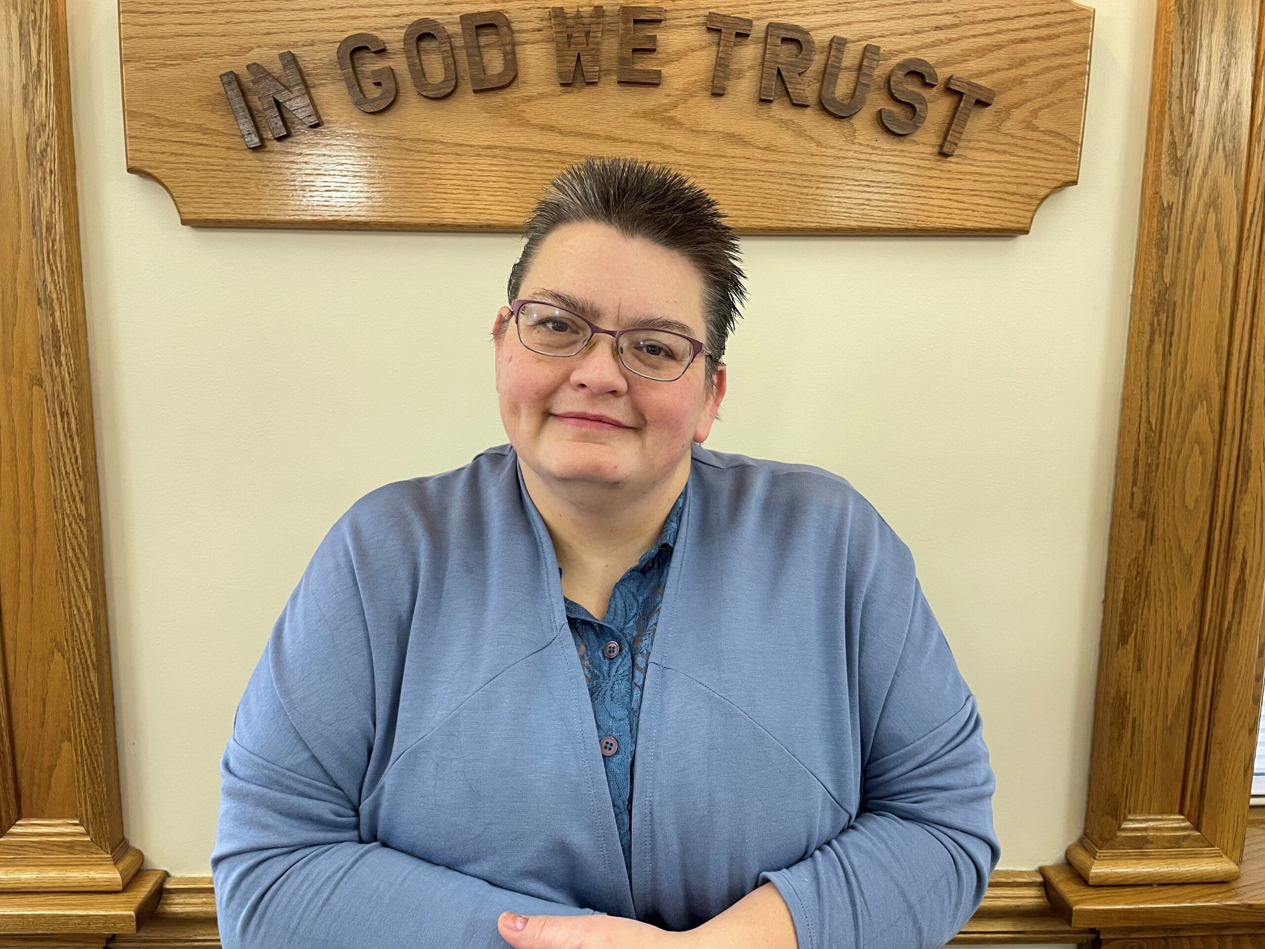 portrait of Tracy in front of in god we trust sign