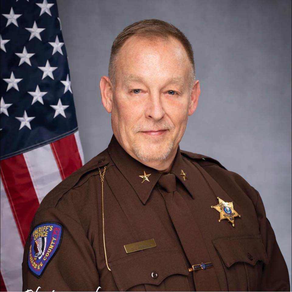 close up portrait of Doug Chapman in sheriff uniform with American flag hanging behind him